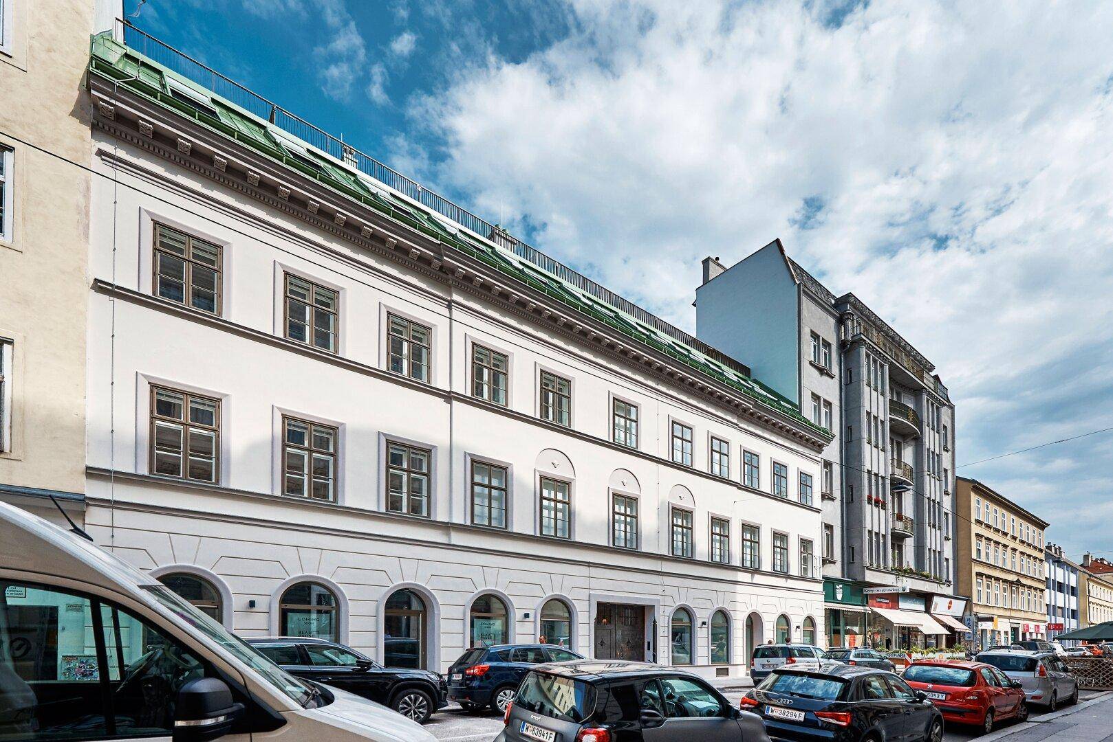 Historische Fassade eines Gebäudes an einer belebten Straße mit parkenden Autos.