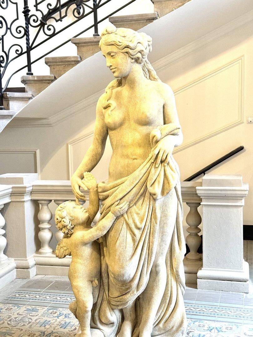 Elegantes Treppenhaus mit einer klassischen Statue, schmiedeeisernem Geländer und gemusterten Fliesen.