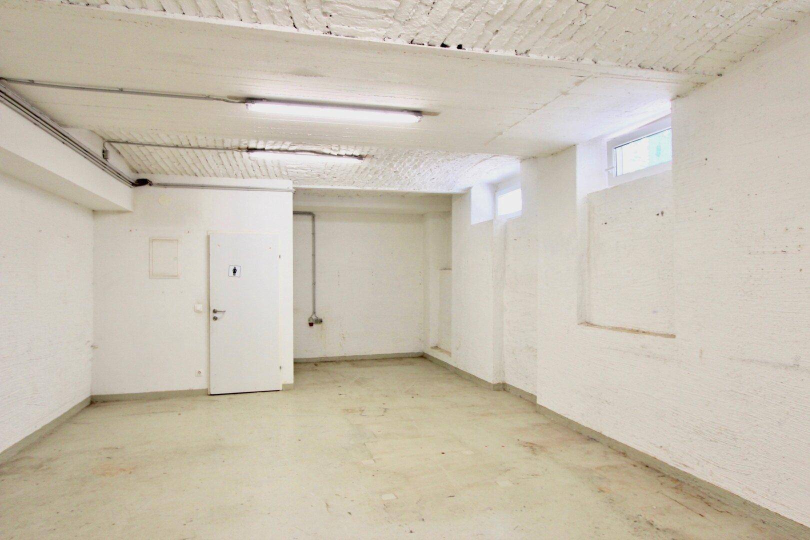 Geräumiger Kellerraum mit weiß gestrichenen Wänden, Betonboden und kleinen Fenstern für Tageslicht.