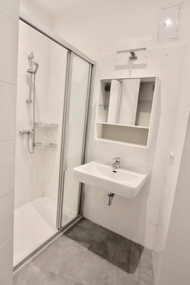 Modernes Badezimmer mit Duschkabine, wandmontiertem Waschbecken und Spiegelschrank, hell gefliest.