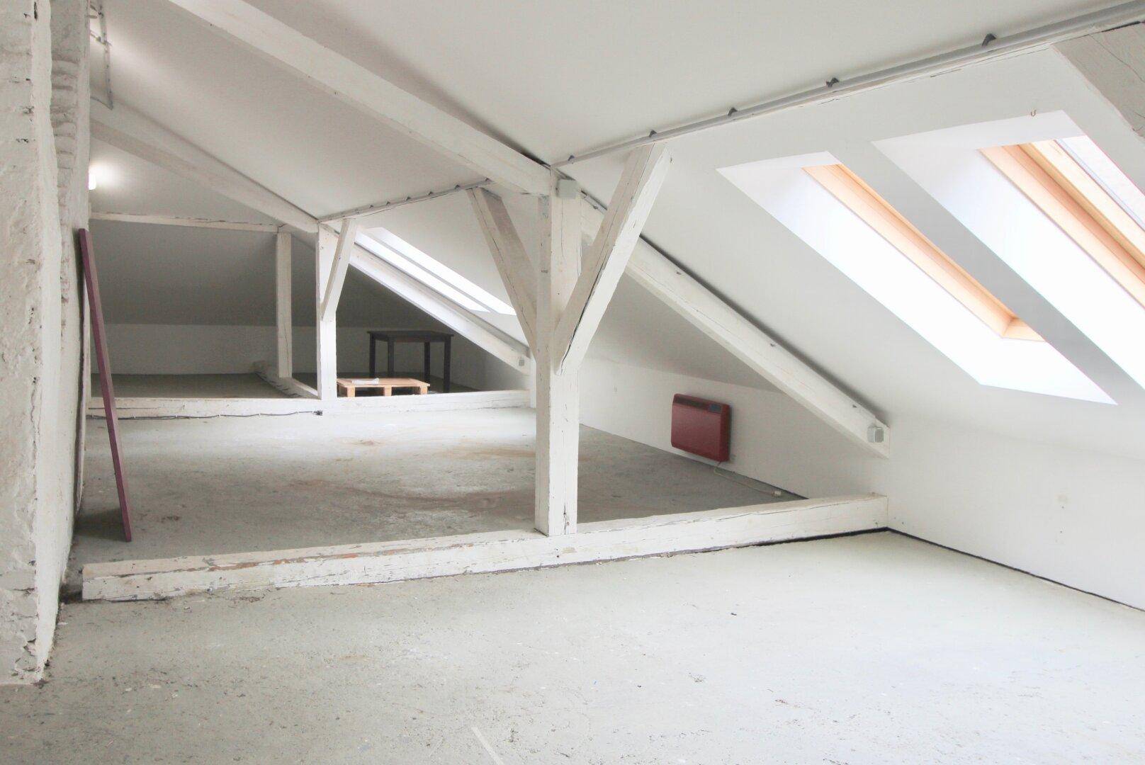 Geräumiger Dachboden mit sichtbaren Holzbalken, schrägen Decken und mehreren Dachfenstern, bereit zum Ausbau.