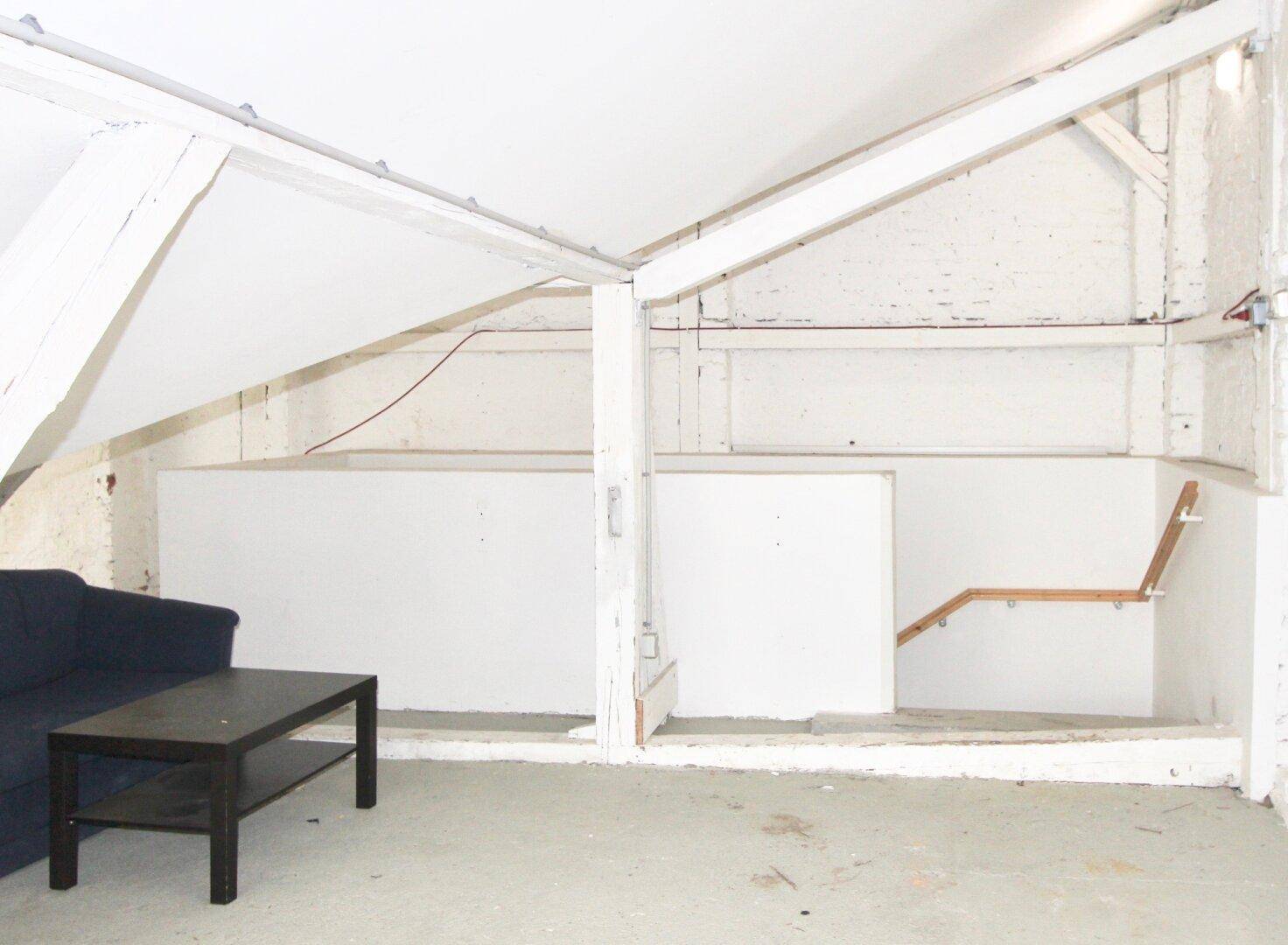 Dachbodenbereich mit schrägen Decken, sichtbaren Holzbalken und einer Sitzecke, die auf den Ausbau wartet.