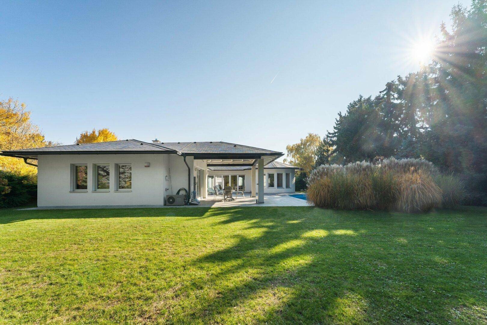 Weitläufiger Gartenbereich mit gepflegtem Rasen und Blick auf die moderne Villa bei Sonnenschein.