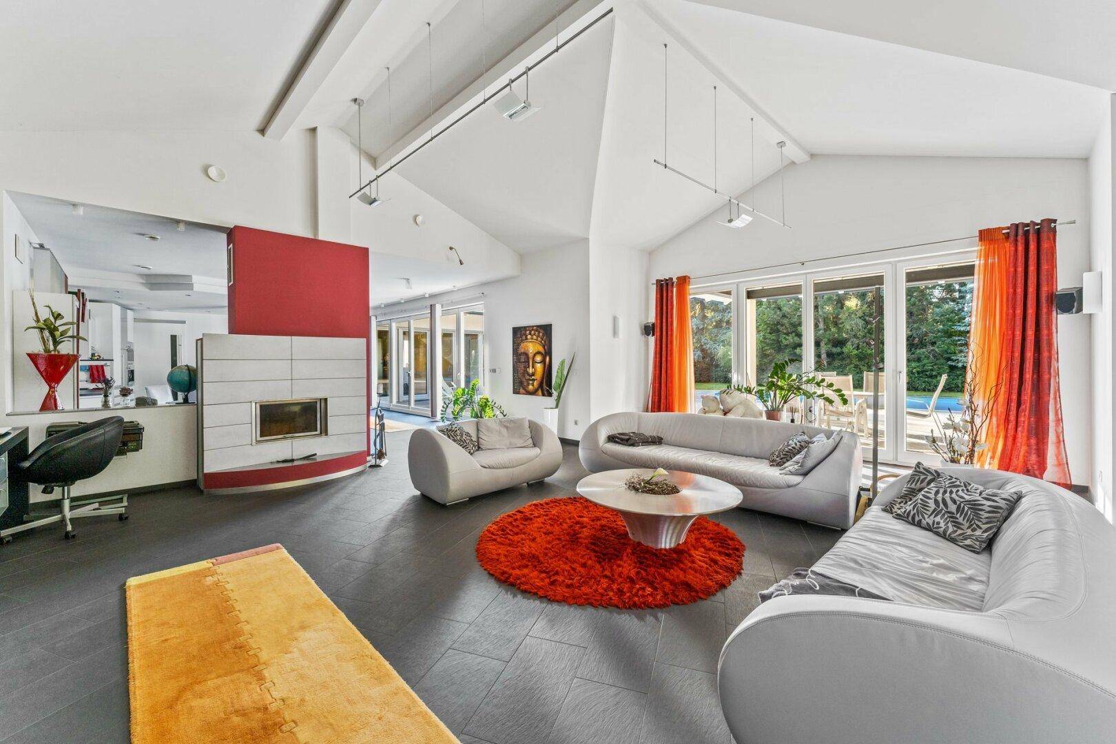 Geräumiges Wohnzimmer mit modernem Kamin, dunklen Fliesen und Zugang zum Gartenbereich.