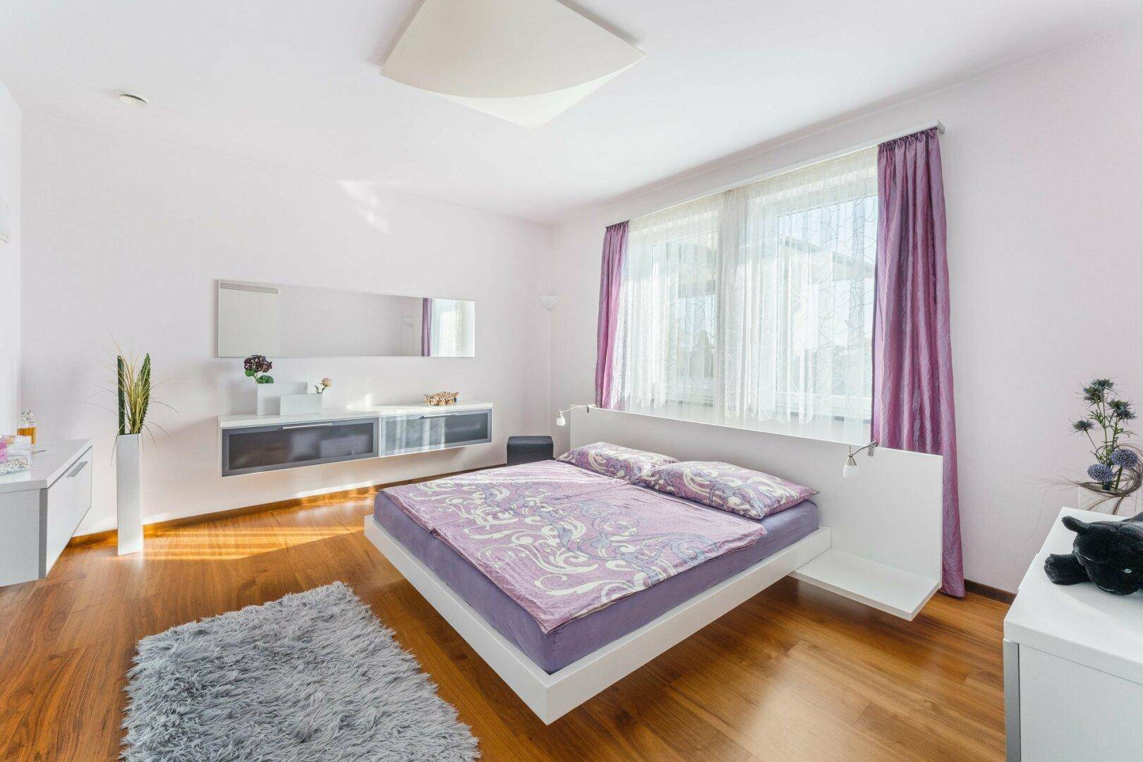 Helles Schlafzimmer mit Holzboden, modernem Bett und großen Fenstern für viel Tageslicht.