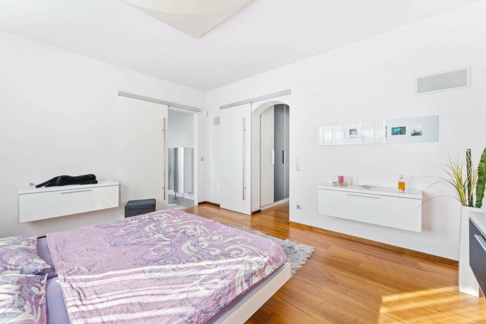 Modernes Schlafzimmer mit Holzboden, schwebendem Bett und Schiebetüren zum Bad.