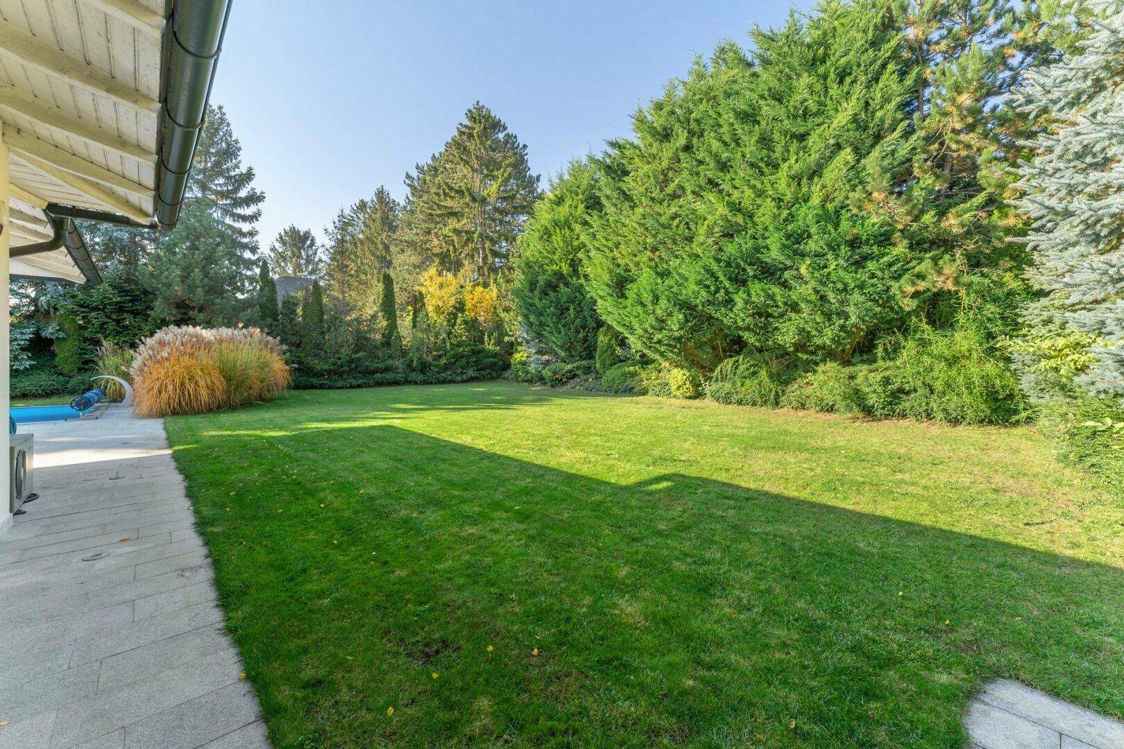 Gepflegter Gartenbereich mit weitläufigem Rasen und üppiger Bepflanzung unter blauem Himmel.