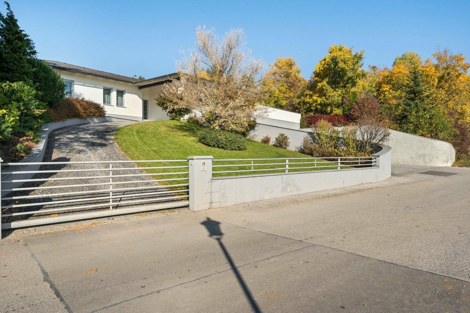 Zufahrt zur modernen Villa mit gepflegter Grünfläche und Einfahrtstor.