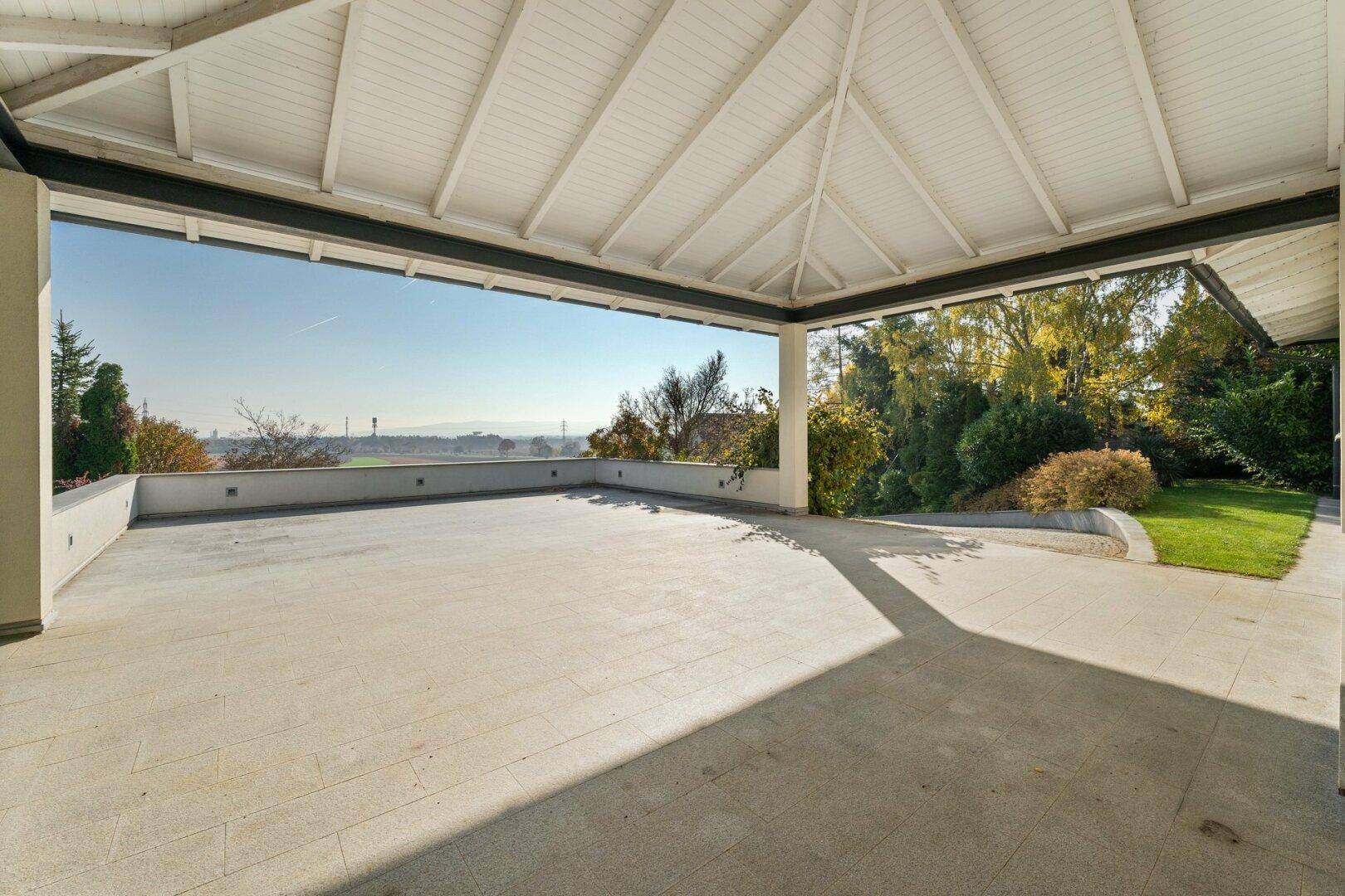 Überdachte Terrasse mit Fliesenboden und offenem Blick in die Natur.