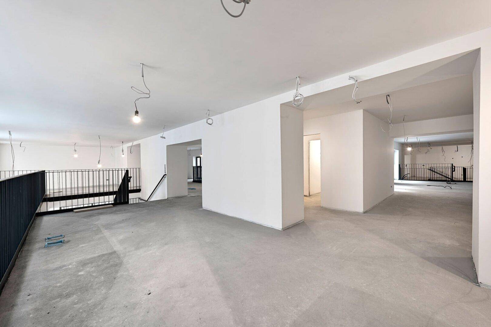 Weitläufiger Bürobereich im Rohbau mit offener Galerie, Betonboden und freiliegenden Kabeln.