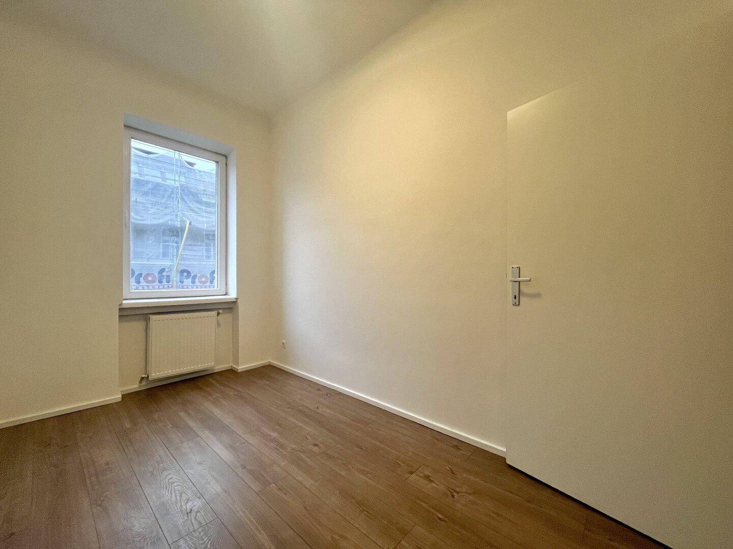 Unmöbliertes Zimmer mit Holzboden und einem Fenster, das viel Tageslicht hereinlässt.