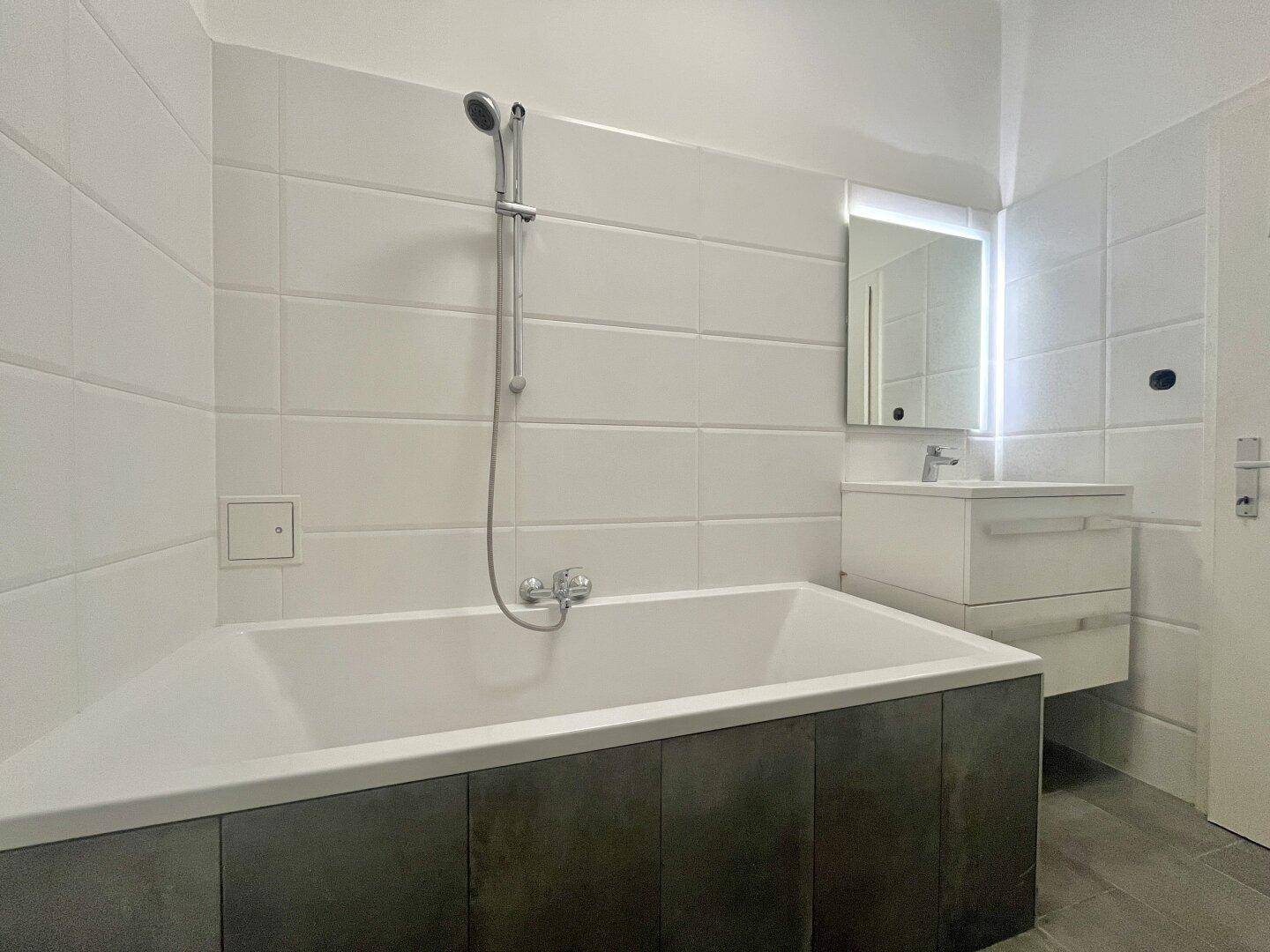 Modernes Badezimmer mit Badewanne, Duscharmatur und einem Waschbecken mit Spiegelschrank.