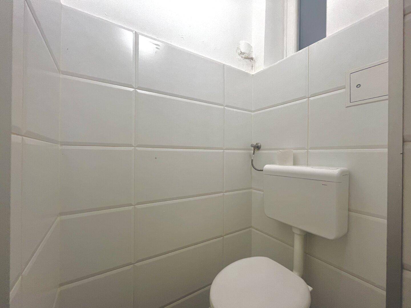 Kleines, gefliestes WC mit Toilette und Spülkasten in sauberem Zustand.