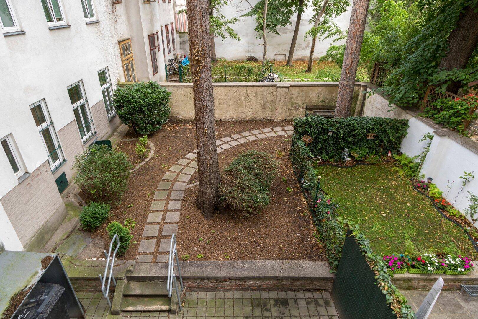 Blick von oben auf einen begrünten Innenhof mit Bäumen und einem gepflasterten Weg.