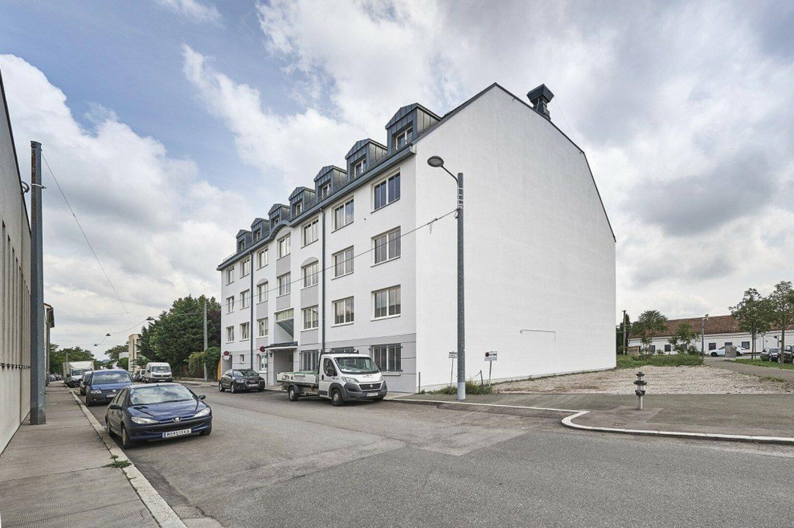Mehrstöckiges Wohngebäude mit weißer Fassade und vielen Fenstern an einer ruhigen Straße.