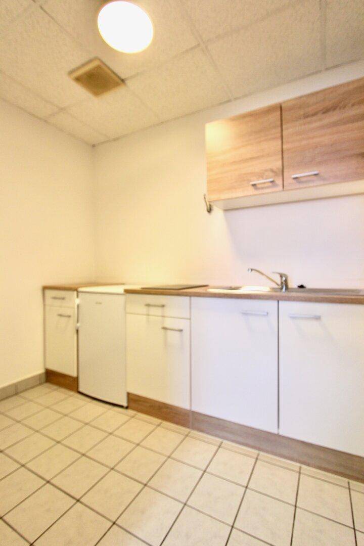 Kleine Küchenzeile mit weißen Unterschränken, Holzoptik-Oberschränken und Fliesenboden.