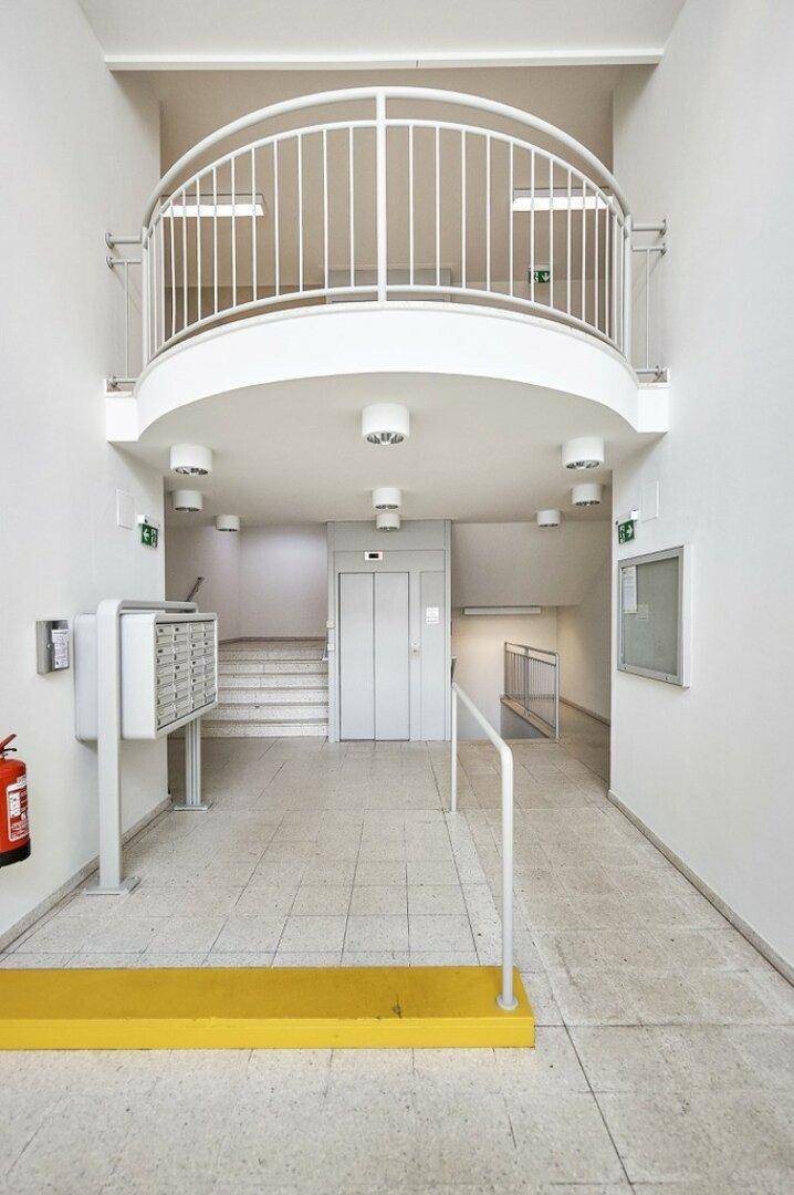 Heller Eingangsbereich mit Aufzug, Treppe und Briefkästen, der Zugang zu den oberen Etagen bietet.
