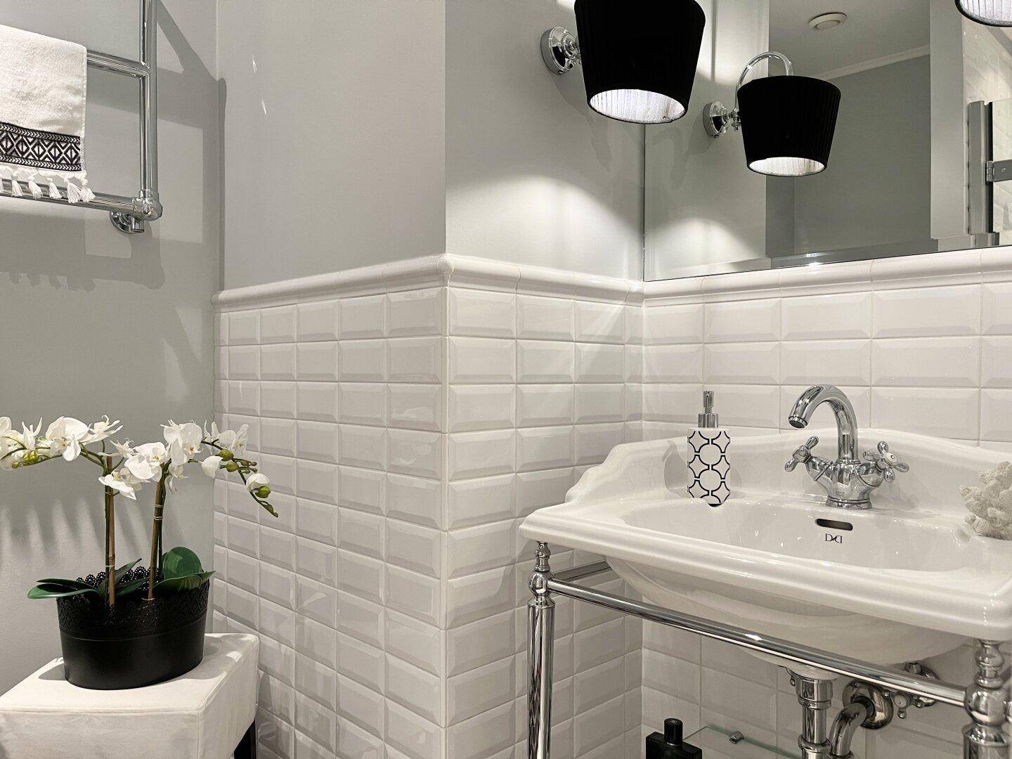 Elegantes Badezimmer mit weißem Waschbecken, Spiegel und dekorativen Wandfliesen.