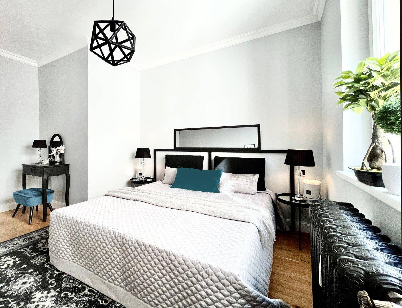 Geräumiges Schlafzimmer mit Holzboden, großem Bett, Schminktisch und Fenster mit Heizkörper.