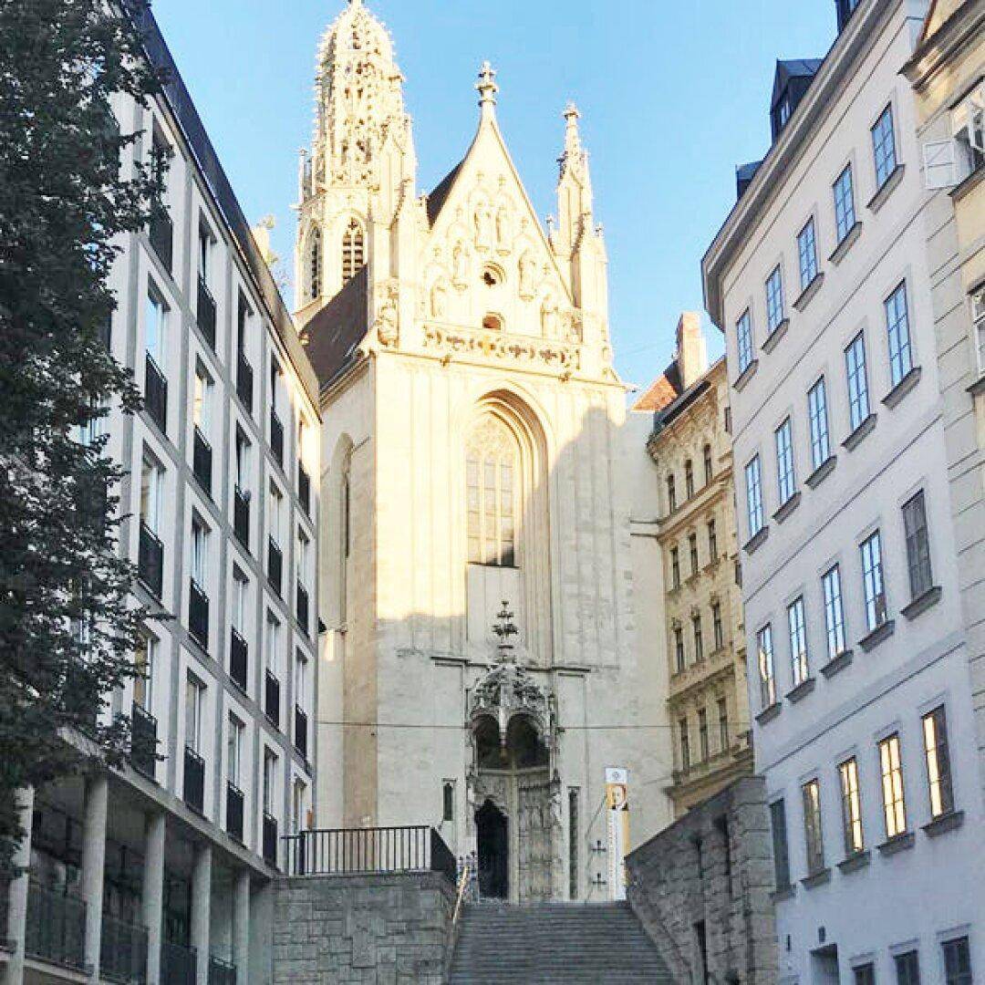 Historische Kirche mit gotischer Architektur, umgeben von städtischen Gebäuden und Bäumen.