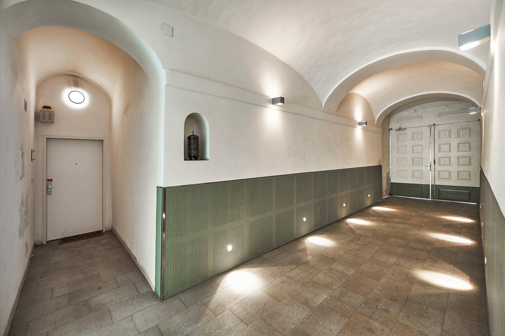 Eingangsbereich mit gewölbter Decke, modernen Wandleuchten und einem Fliesenboden.