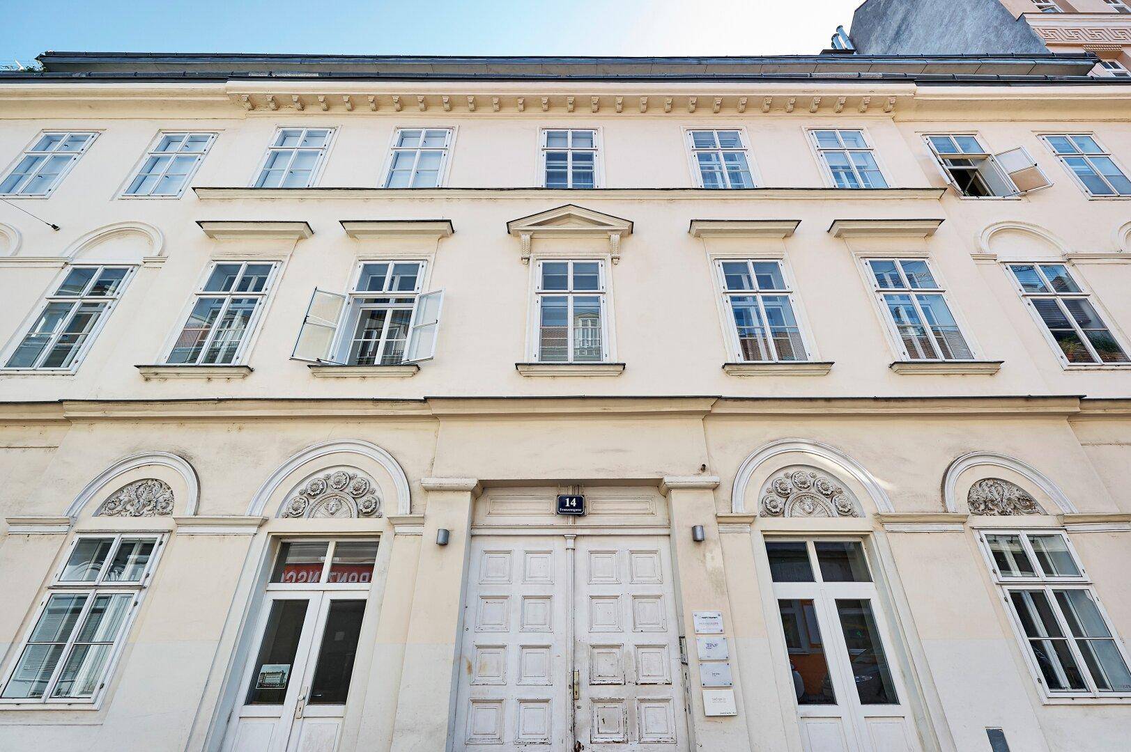 Historische Fassade eines Altbaus mit vielen Fenstern, dekorativen Elementen und einer großen Eingangstür.