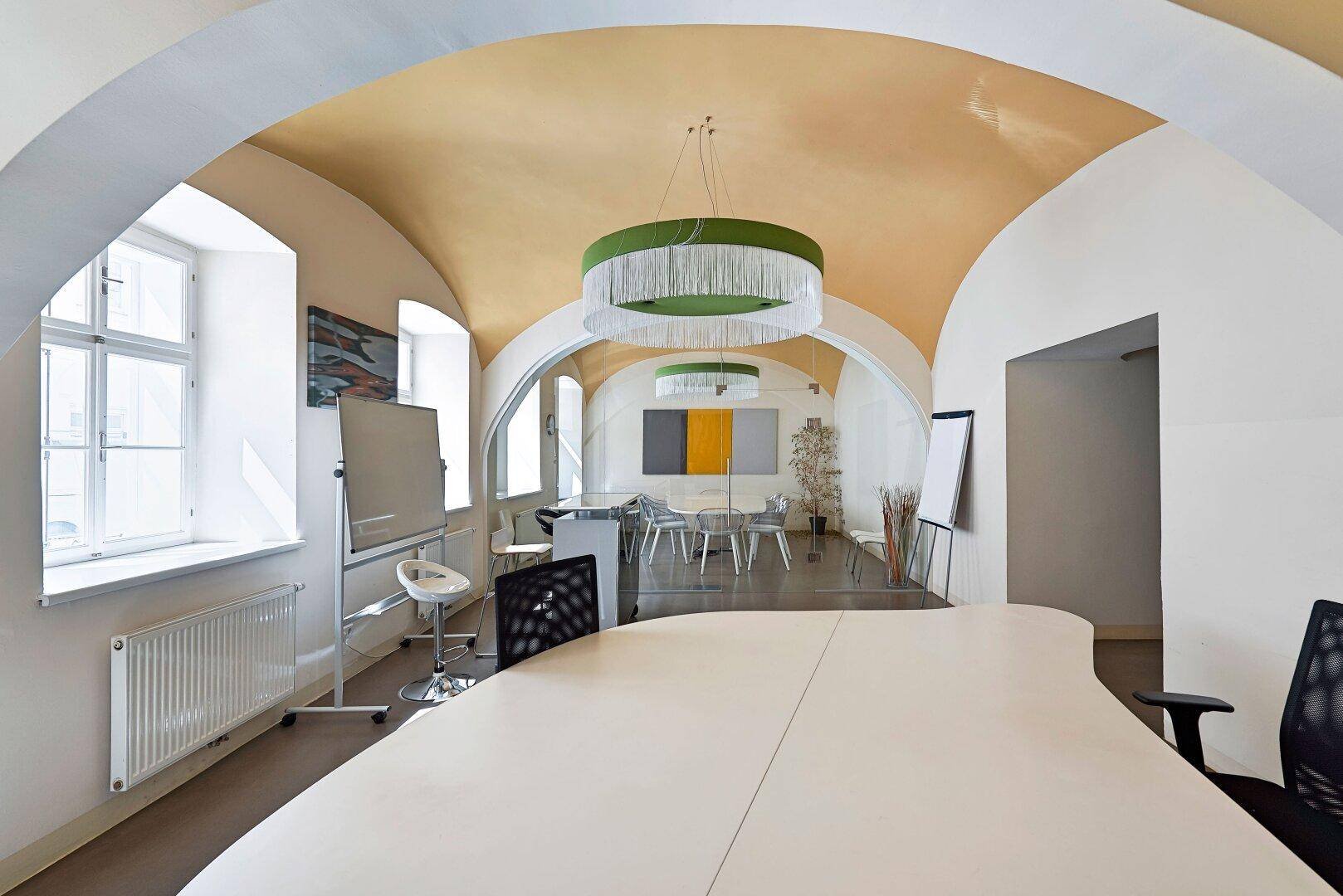 Helles Büro mit stilvoller Gewölbedecke, modernen Leuchten und großen Fenstern mit Blick ins Grüne.
