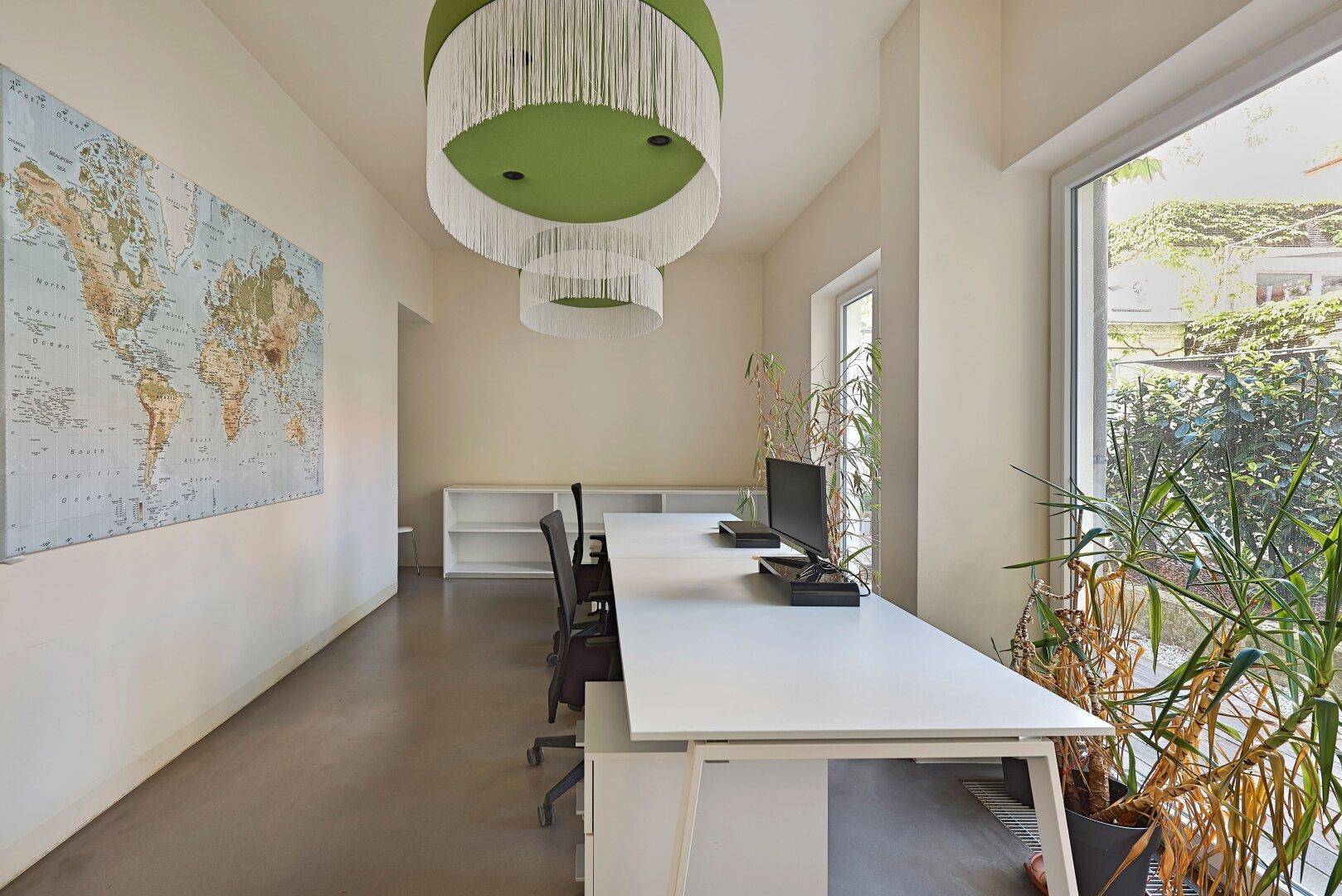 Lichtdurchfluteter Büroraum mit einer großen Weltkarte, modernem Schreibtisch und Zimmerpflanzen.