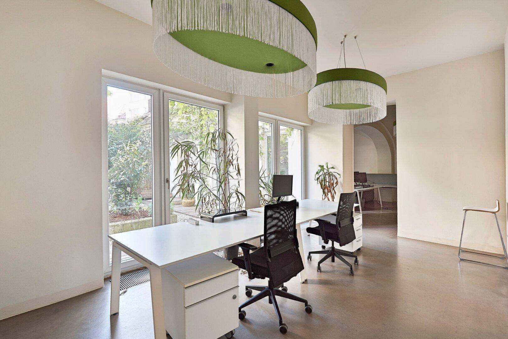 Moderner Bürobereich mit großen Fenstern, grünen Pflanzen und zeitgenössischer Einrichtung.