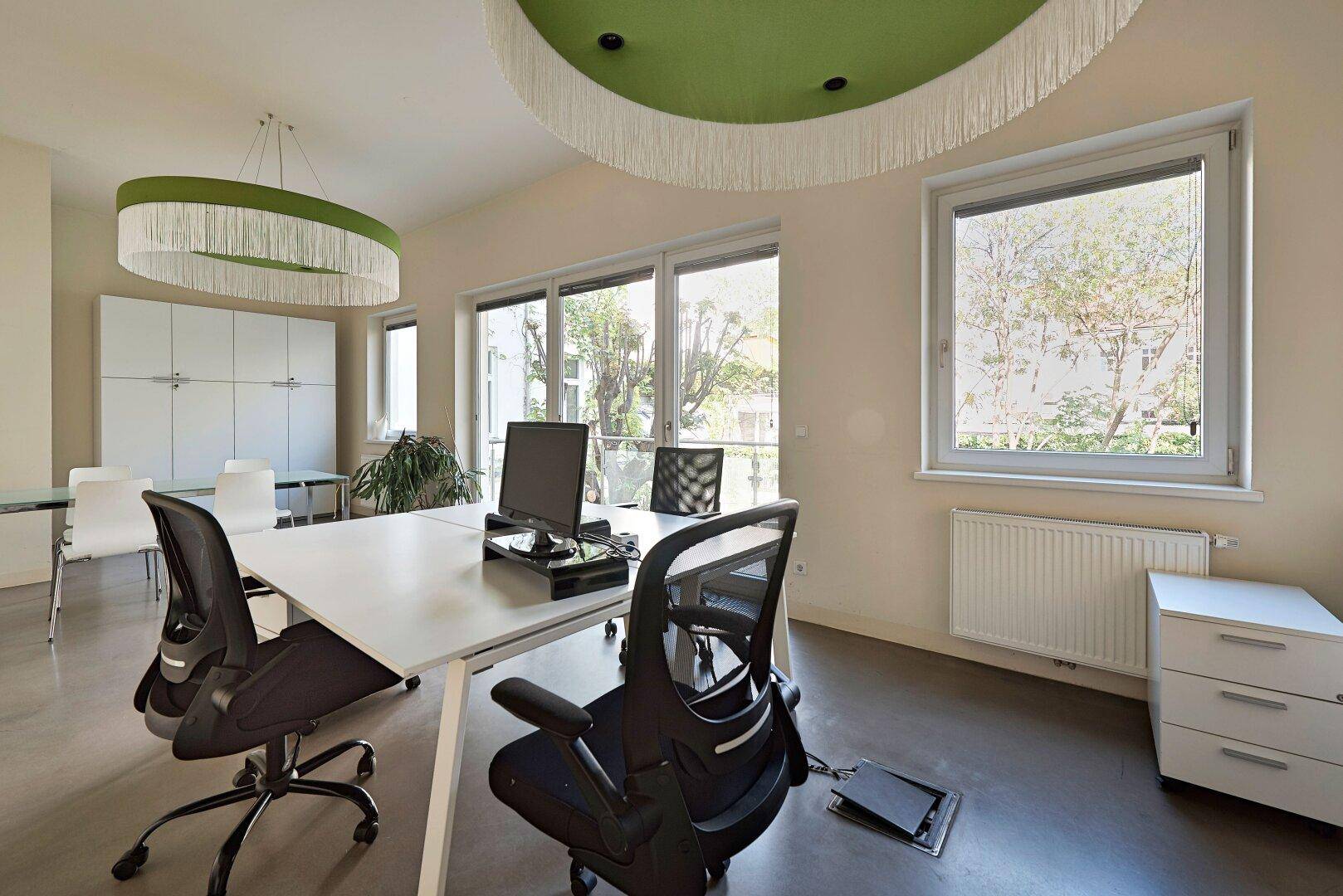 Heller Büroraum mit großem Fenster, Heizkörper und modernem Schreibtisch mit Bürostuhl.