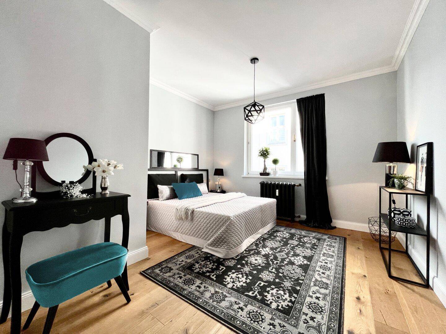 Helles Schlafzimmer mit Holzboden, großem Bett, Schminktisch und dekorativem Teppich.