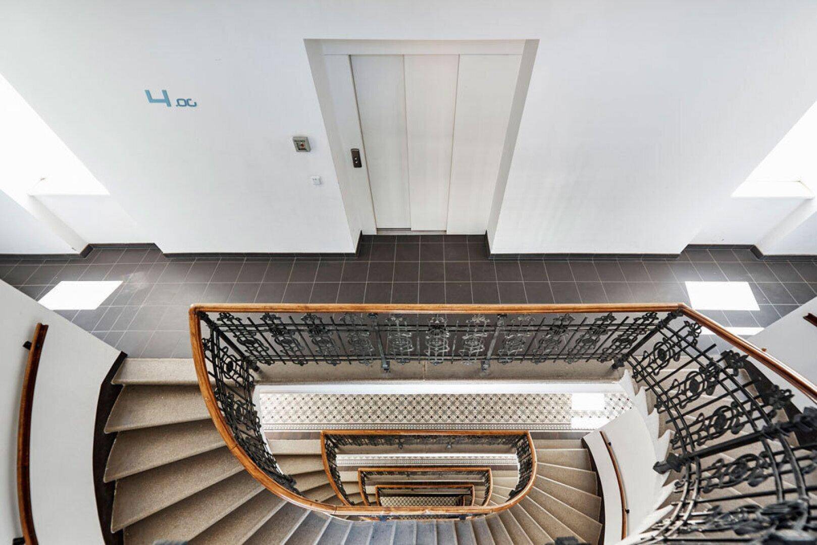 Wendeltreppe mit schmiedeeisernem Geländer und Aufzug im Treppenhaus eines Altbaus.