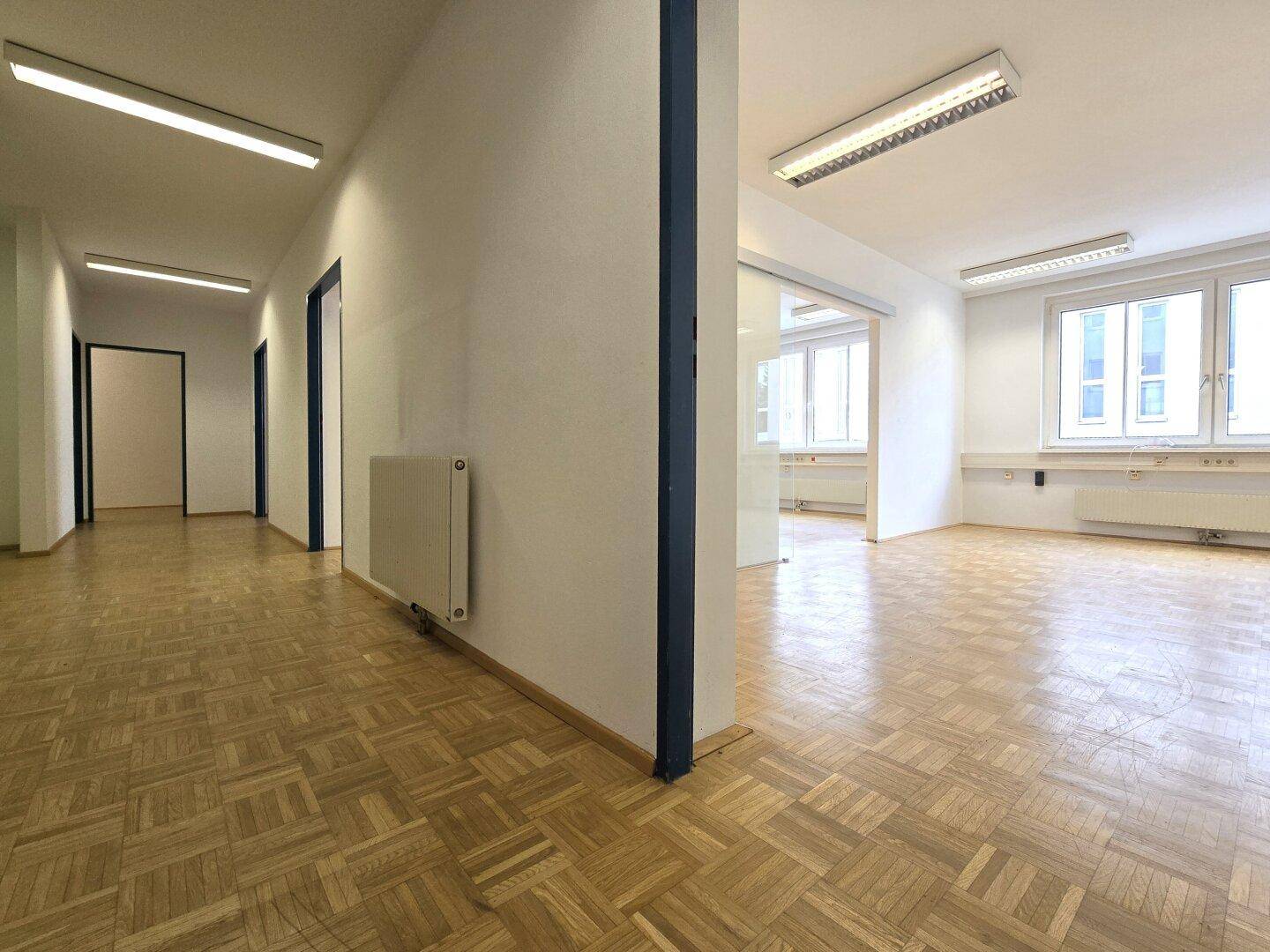 Heller Flur mit Parkettboden, der zu mehreren Büroräumen und einem offenen Bereich führt.