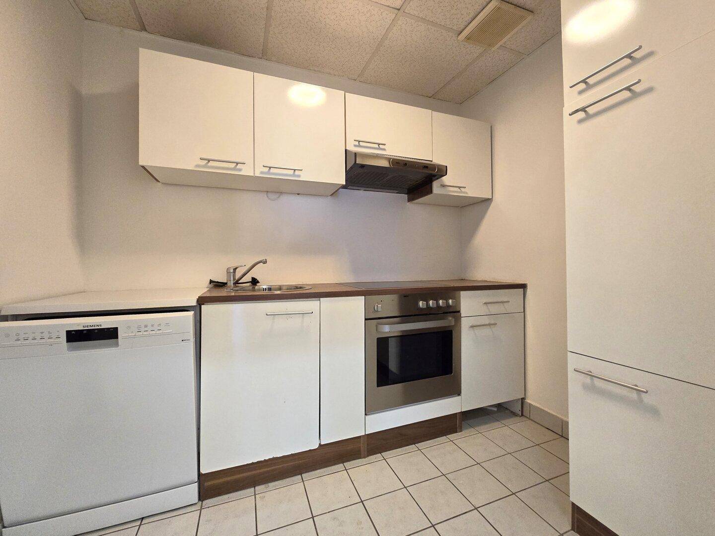 Funktionale Küchenzeile mit weißen Schränken, Spülmaschine und Backofen, ideal für Büroräume.