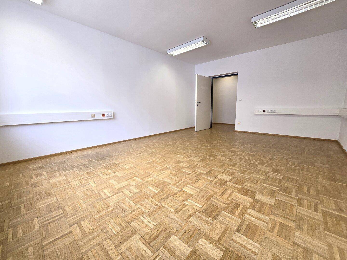 Leeres Büro mit Parkettboden und weißen Wänden, bereit für individuelle Gestaltung und Nutzung.