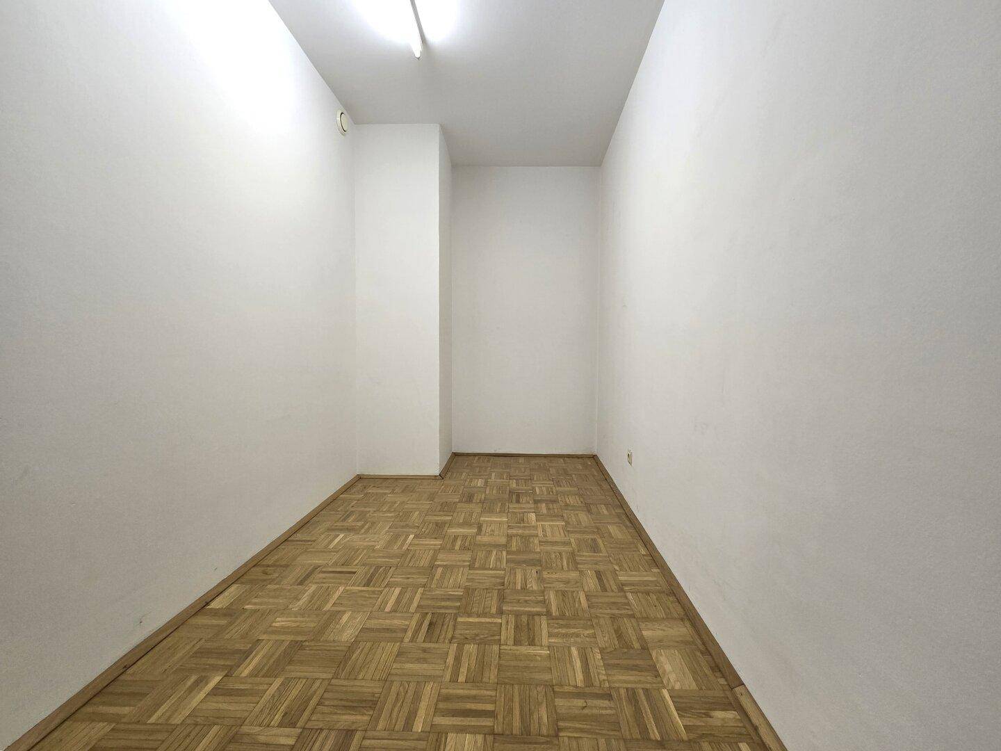 Schmaler, leerer Raum mit Parkettboden und weißen Wänden, geeignet als Abstellkammer oder Archiv.