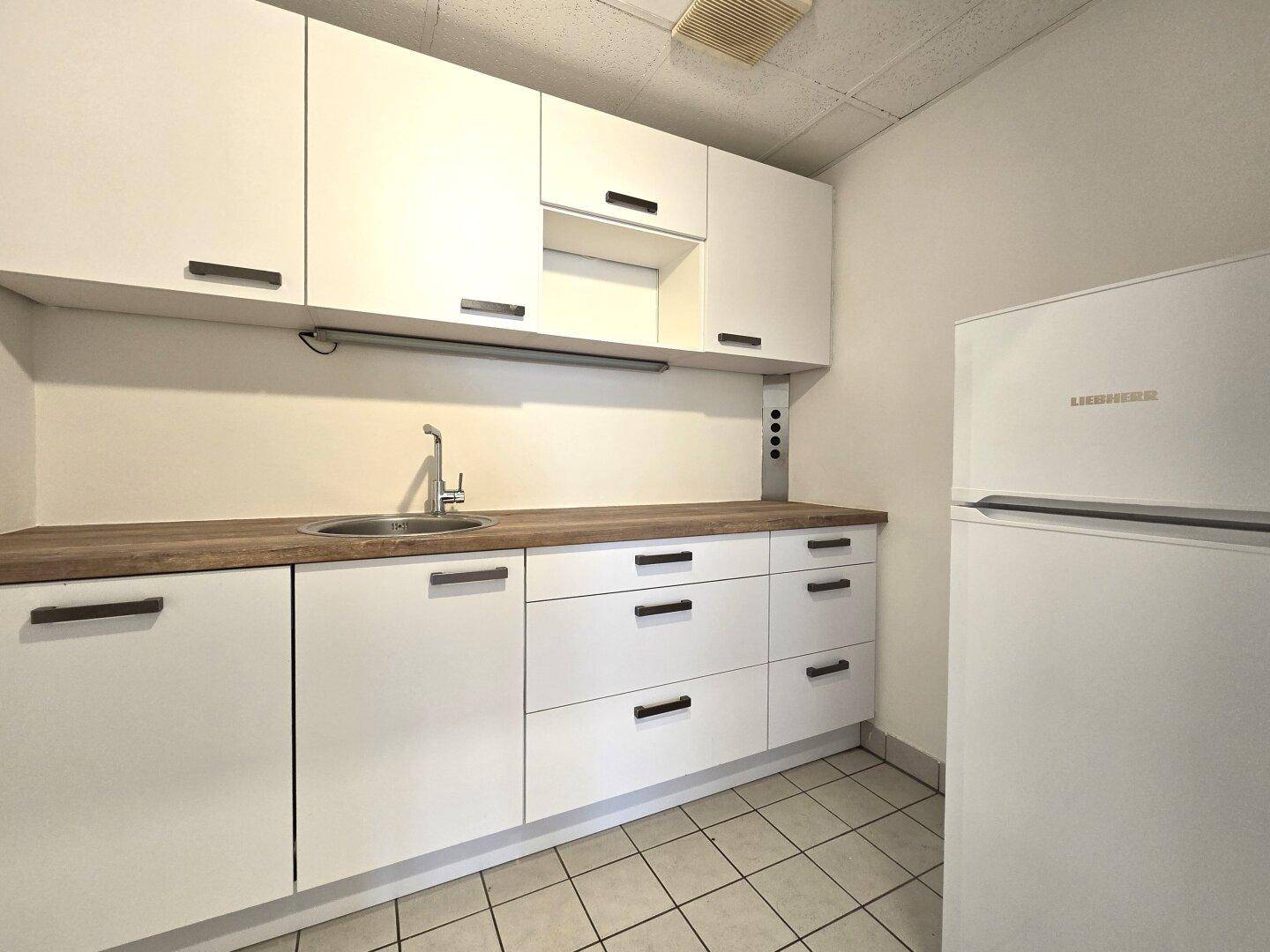 Kleine, funktionale Teeküche mit weißen Schränken, Holz-Arbeitsplatte, Spüle und Kühlschrank.