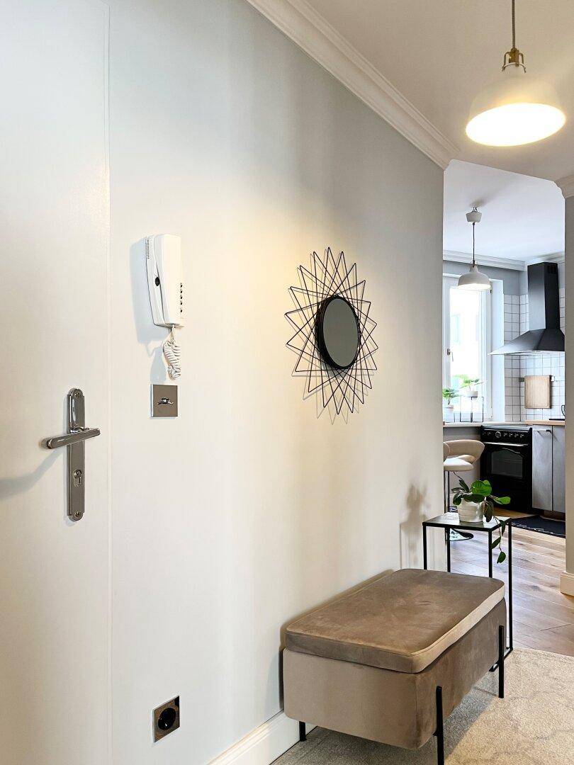 Eingangsbereich mit Holzboden, modernem Spiegel und Gegensprechanlage an der Wand.