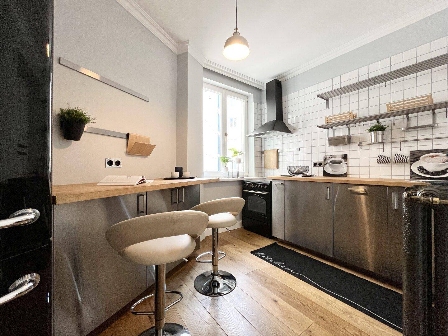 Moderne Küche mit Edelstahlfronten, Holzarbeitsplatte und Frühstücksbar am Fenster.