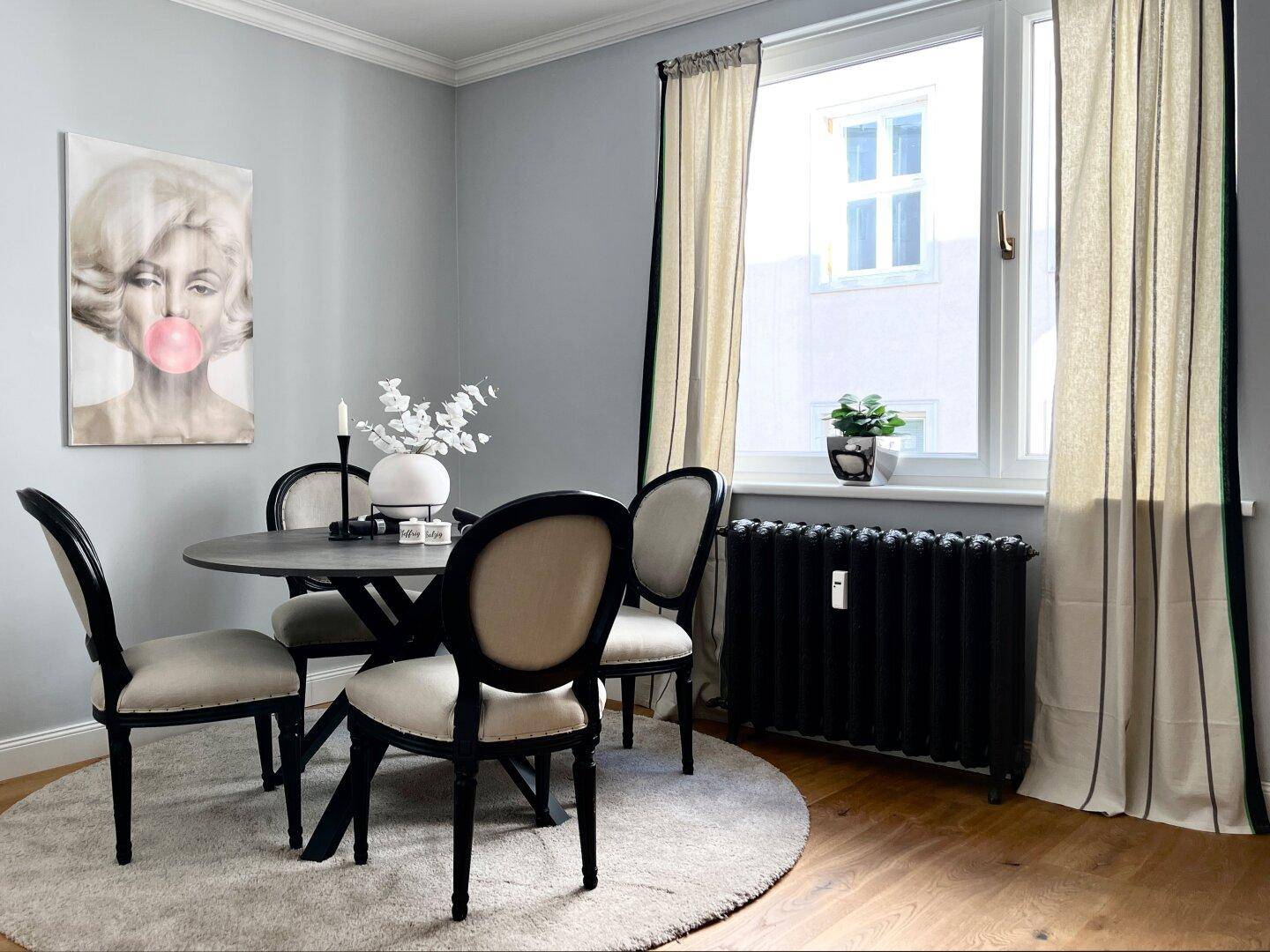 Essbereich mit rundem Tisch, eleganten Stühlen und großem Fenster mit Vorhängen.