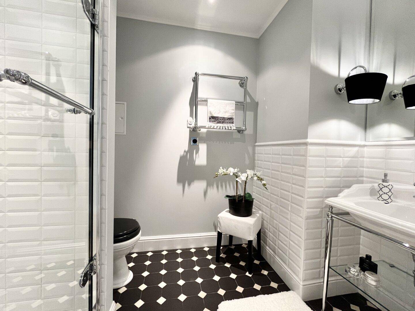 Modernes Badezimmer mit schwarz-weißem Fliesenboden, Dusche und beheiztem Handtuchhalter.