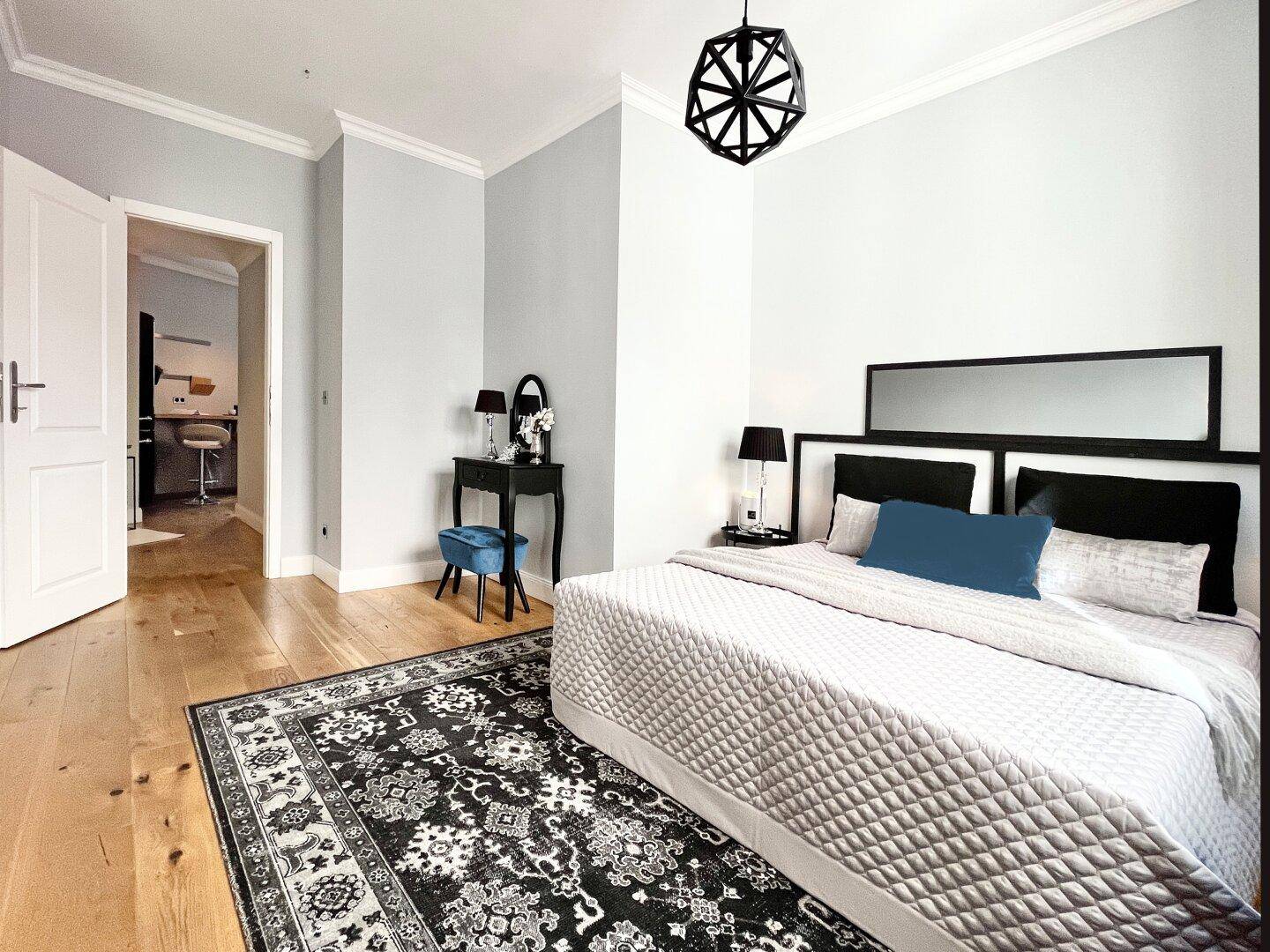 Schlafzimmer mit Holzboden, großem Bett und Blick in den angrenzenden Flur.