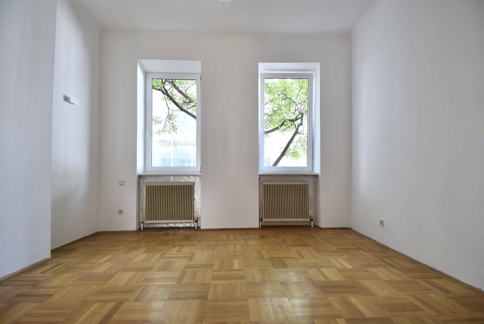 Helles Zimmer mit Fischgrätparkett und Blick ins Grüne, ideal als Schlafzimmer.