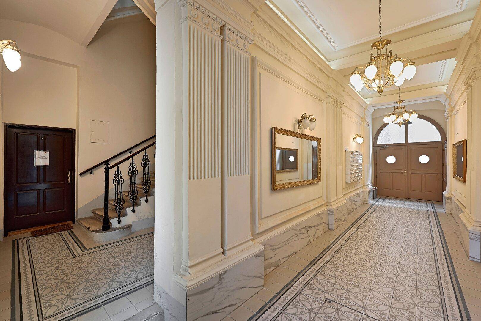 Elegante Eingangshalle mit historischem Treppenhaus, Stuckelementen und gemusterten Fliesenboden.