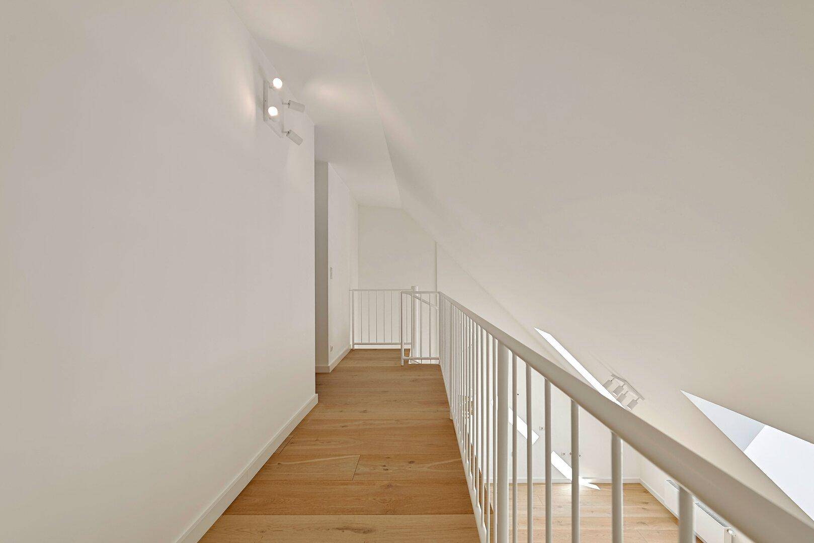 Heller Flur auf der Galerieebene mit Holzfußboden und Blick in den darunterliegenden Wohnbereich.