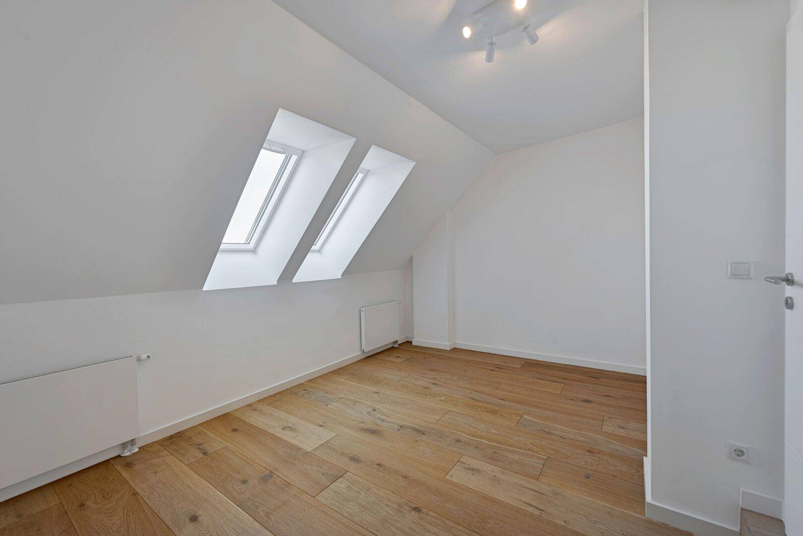 Geräumiges Schlafzimmer im Dachgeschoss mit Holzfußboden, weißen Wänden und Dachfenstern.
