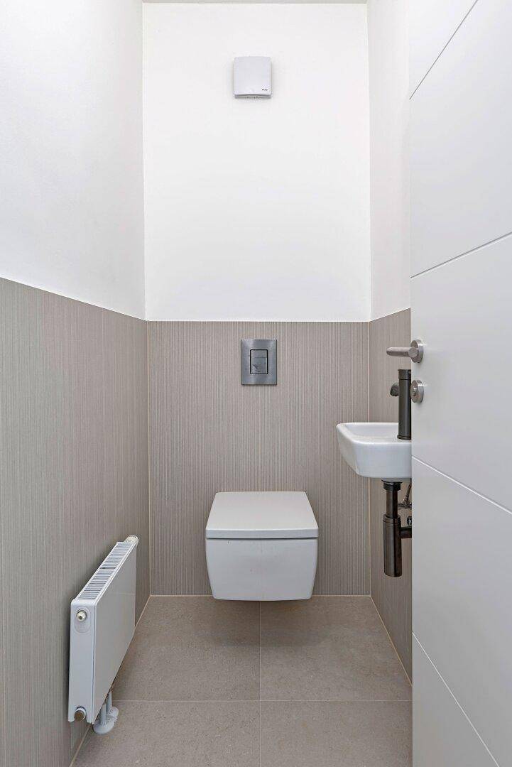 Modernes Gäste-WC mit wandhängendem WC, kleinem Waschbecken und beigefarbenen Fliesen.