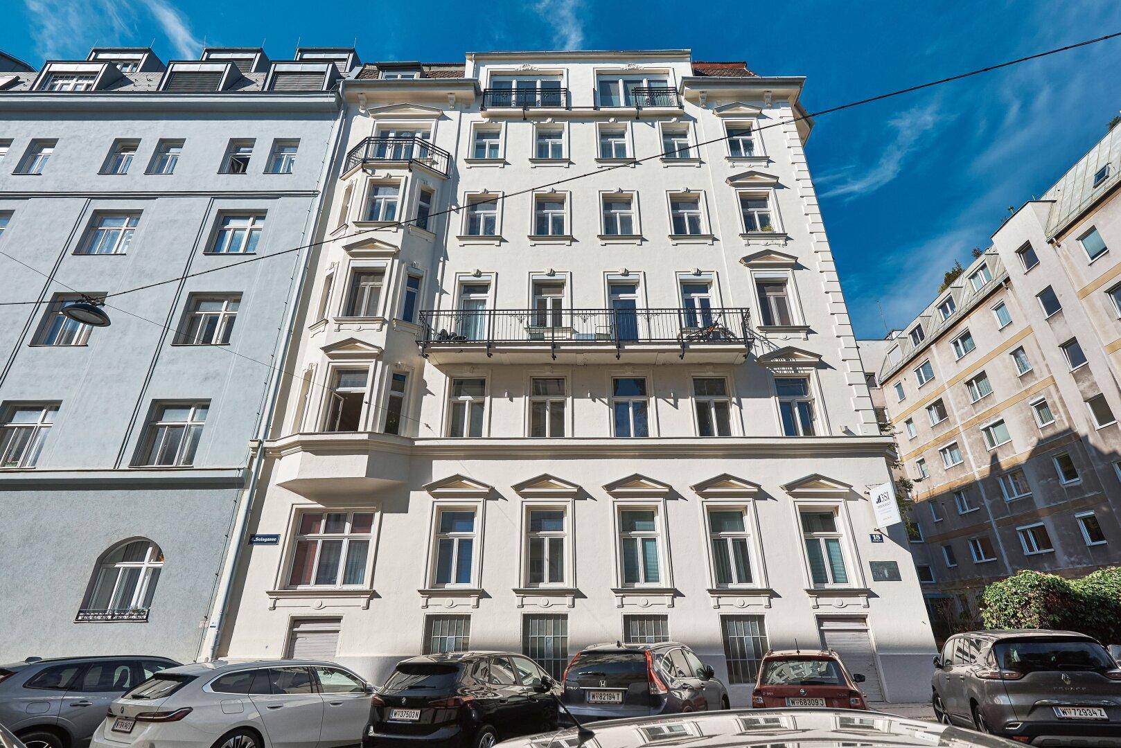 Vorderansicht eines klassischen Wohnhauses mit mehreren Etagen und Balkonen an einer belebten Straße.