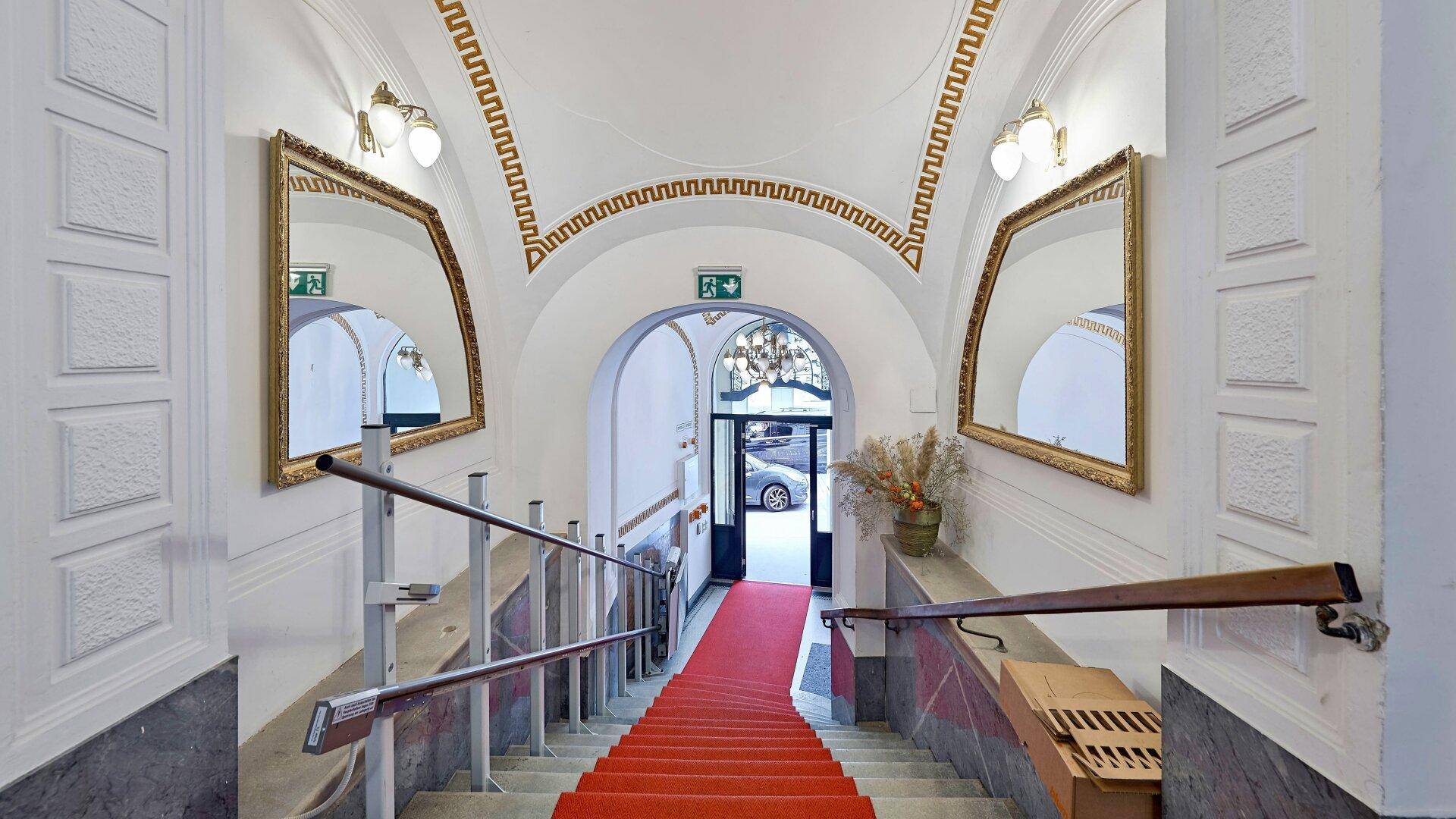 Prunkvolles Treppenhaus mit rotem Teppich, Marmorwänden und einem Treppenlift.