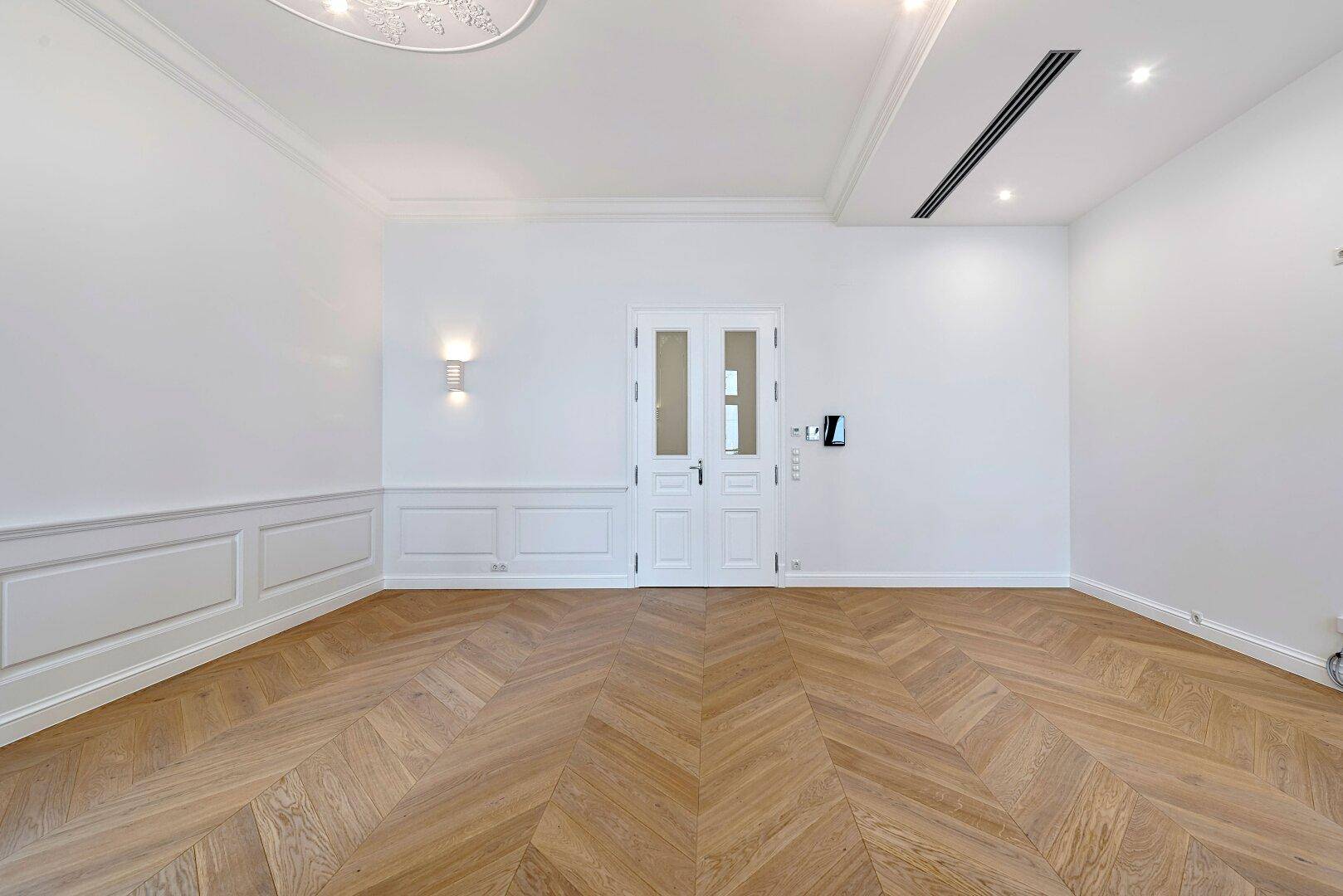 Geräumiges Zimmer mit Fischgrätparkett, hohen Decken und stilvollen Wandpaneelen.